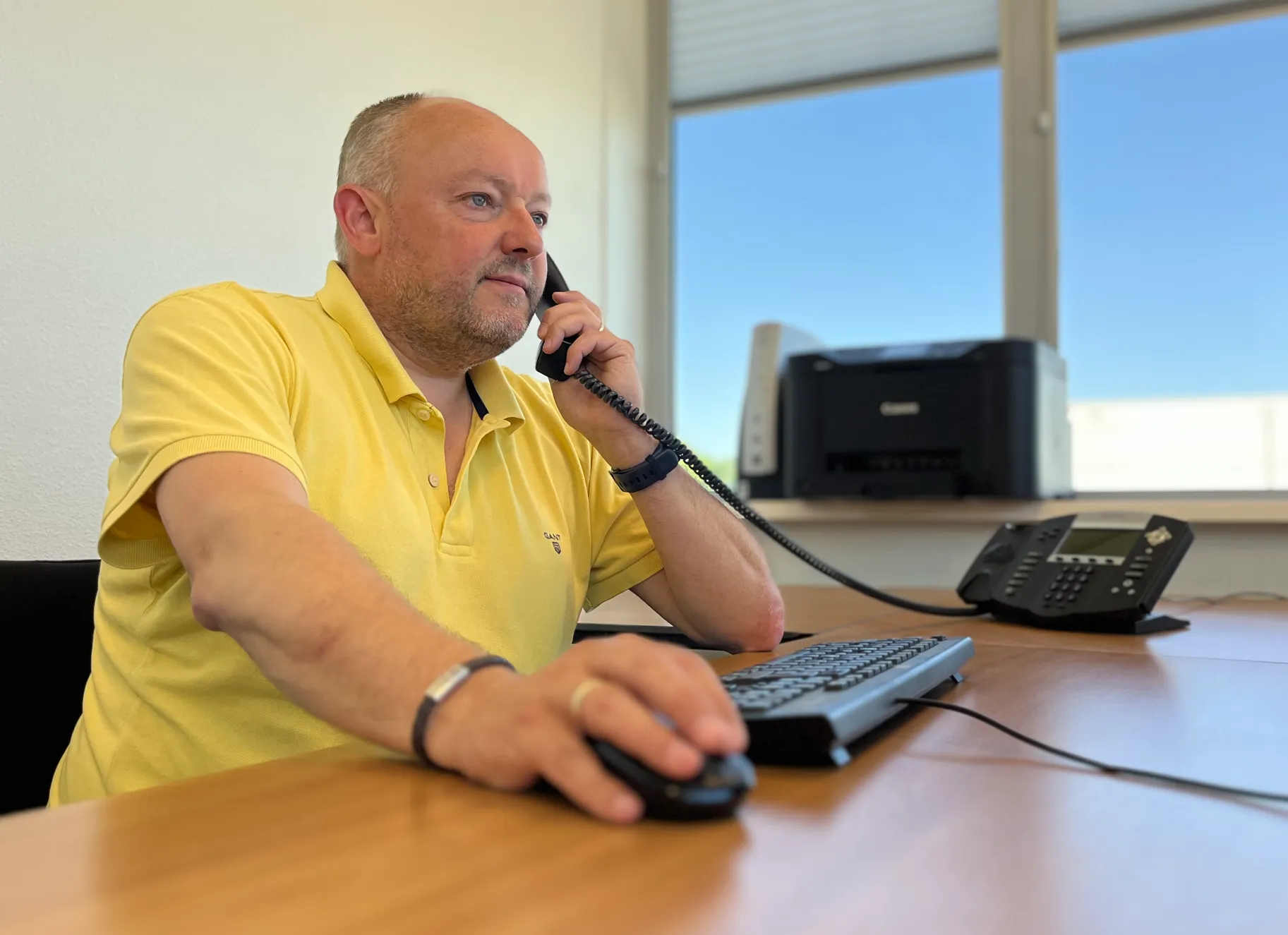 Foto toont Henri achter het bureau met aan de telefoon.