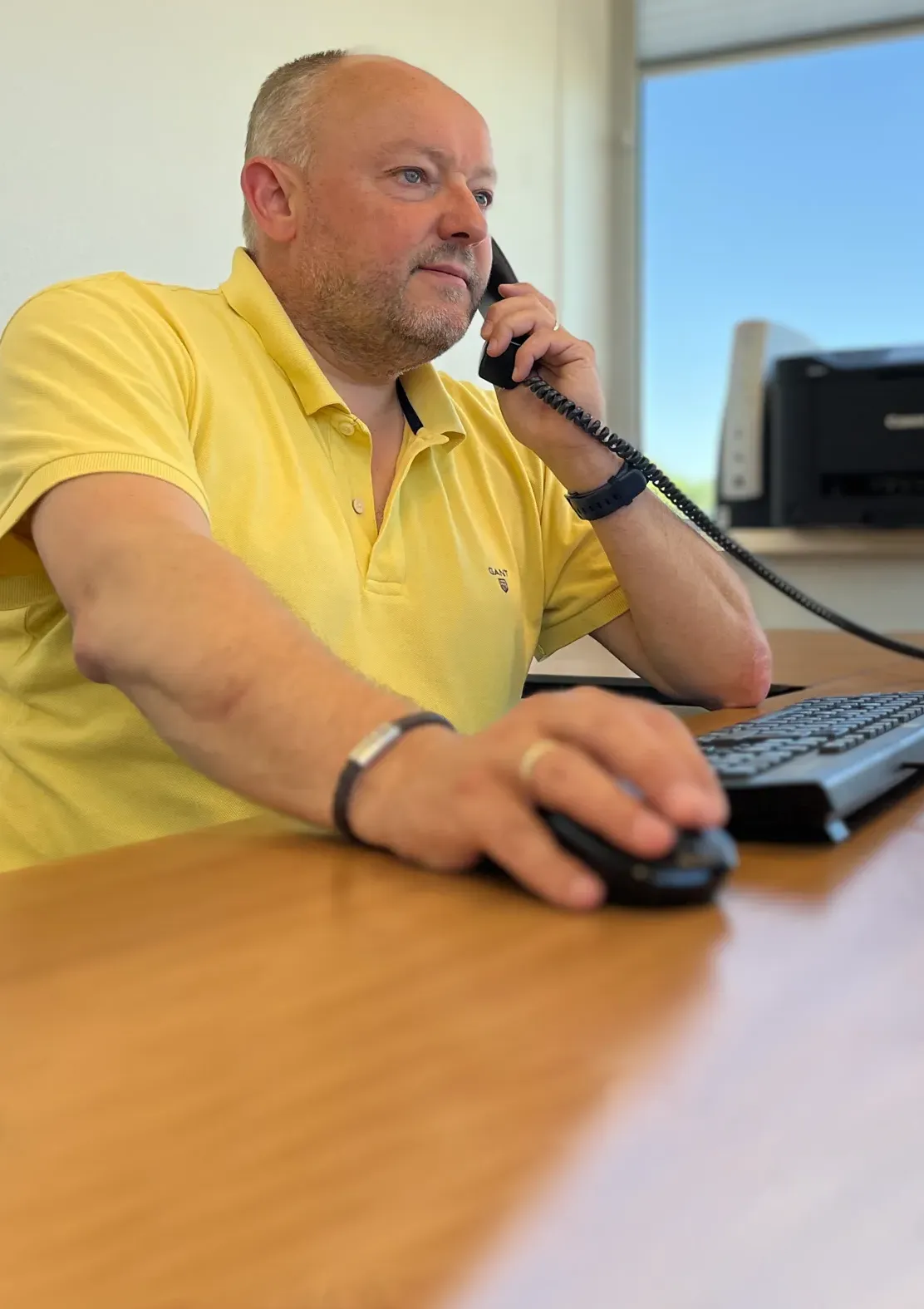 Foto toont Henri achter het bureau met aan de telefoon.